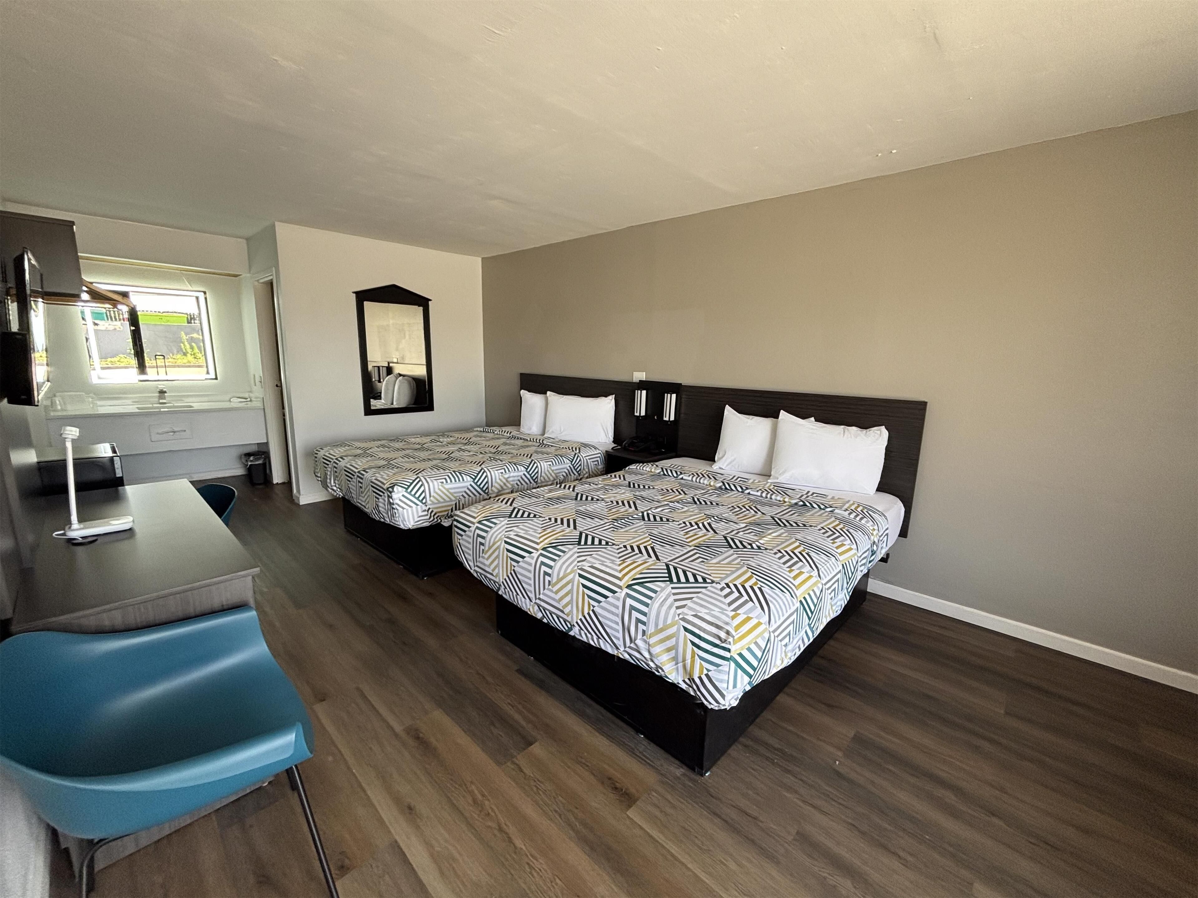 A hotel room with two beds, a desk, and a chair.