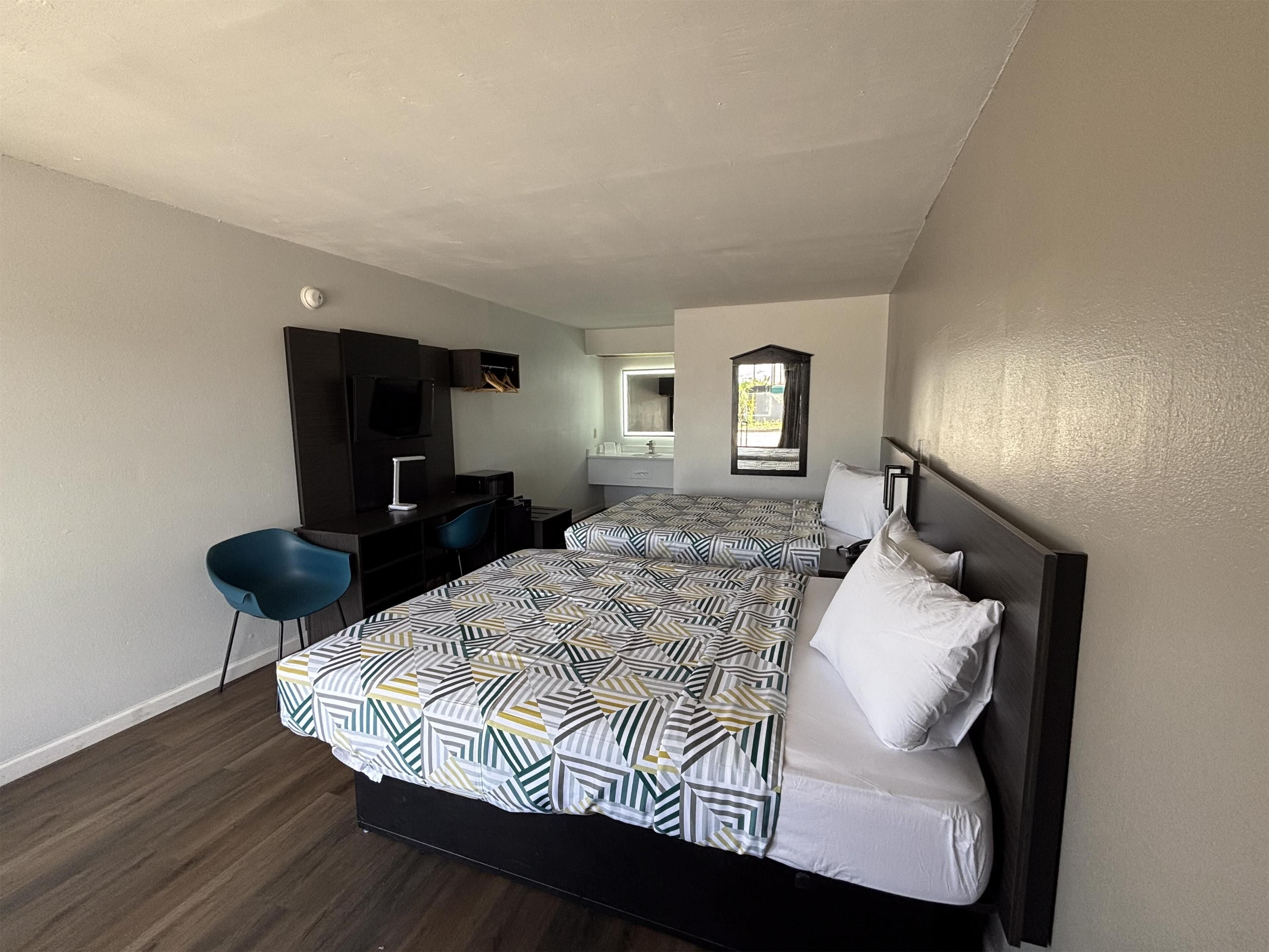 Hotelkamer met twee bedden, een bureau, een stoel, een televisie en een badkamer zichtbaar door een geopende deur.