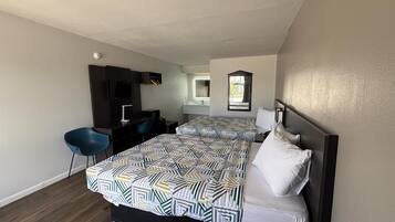 Habitación de hotel con dos camas, un escritorio, una silla, un televisor y un baño visible a través de una puerta abierta.