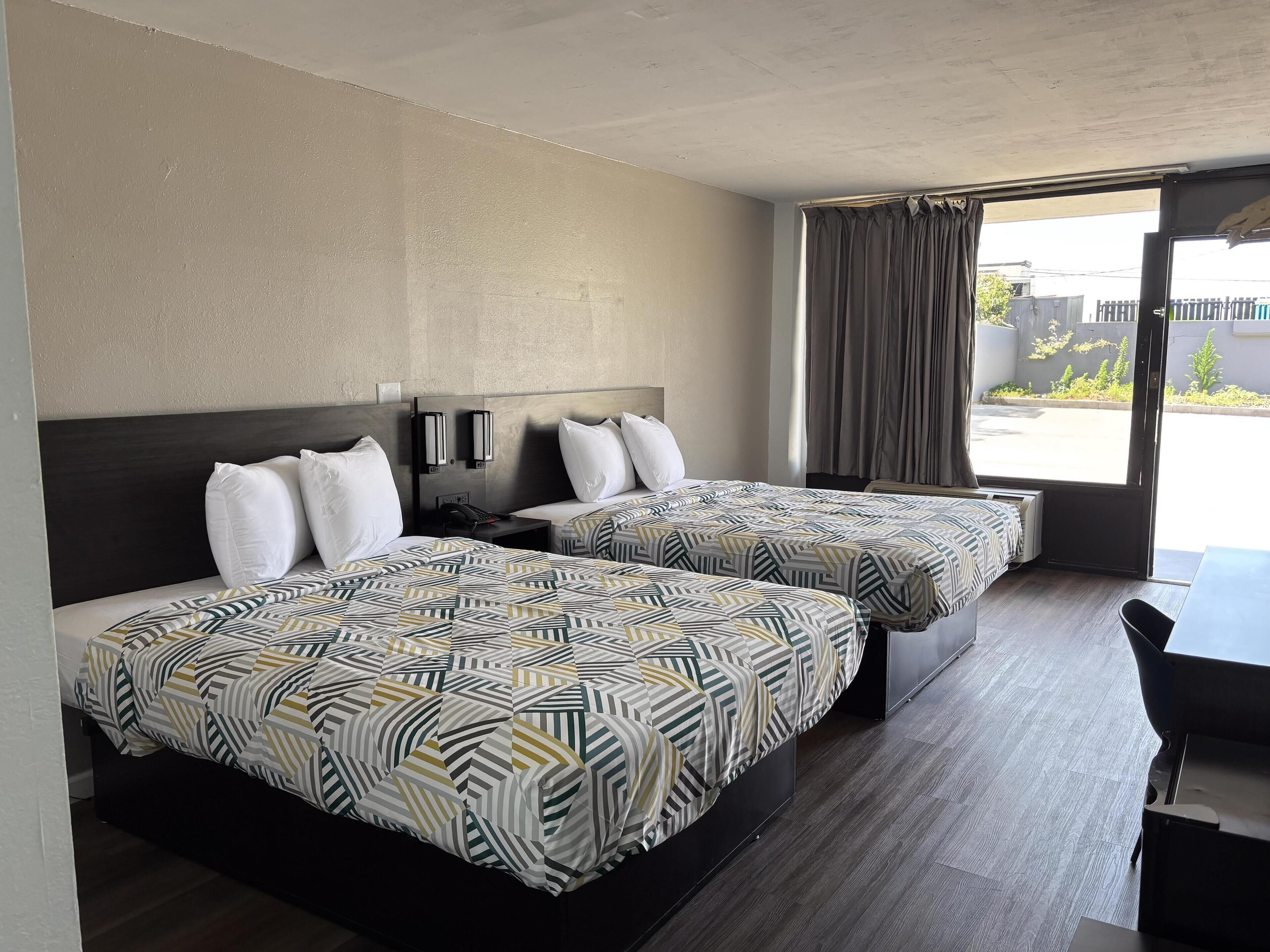 A hotel room with two beds, a desk, and a large window with curtains.