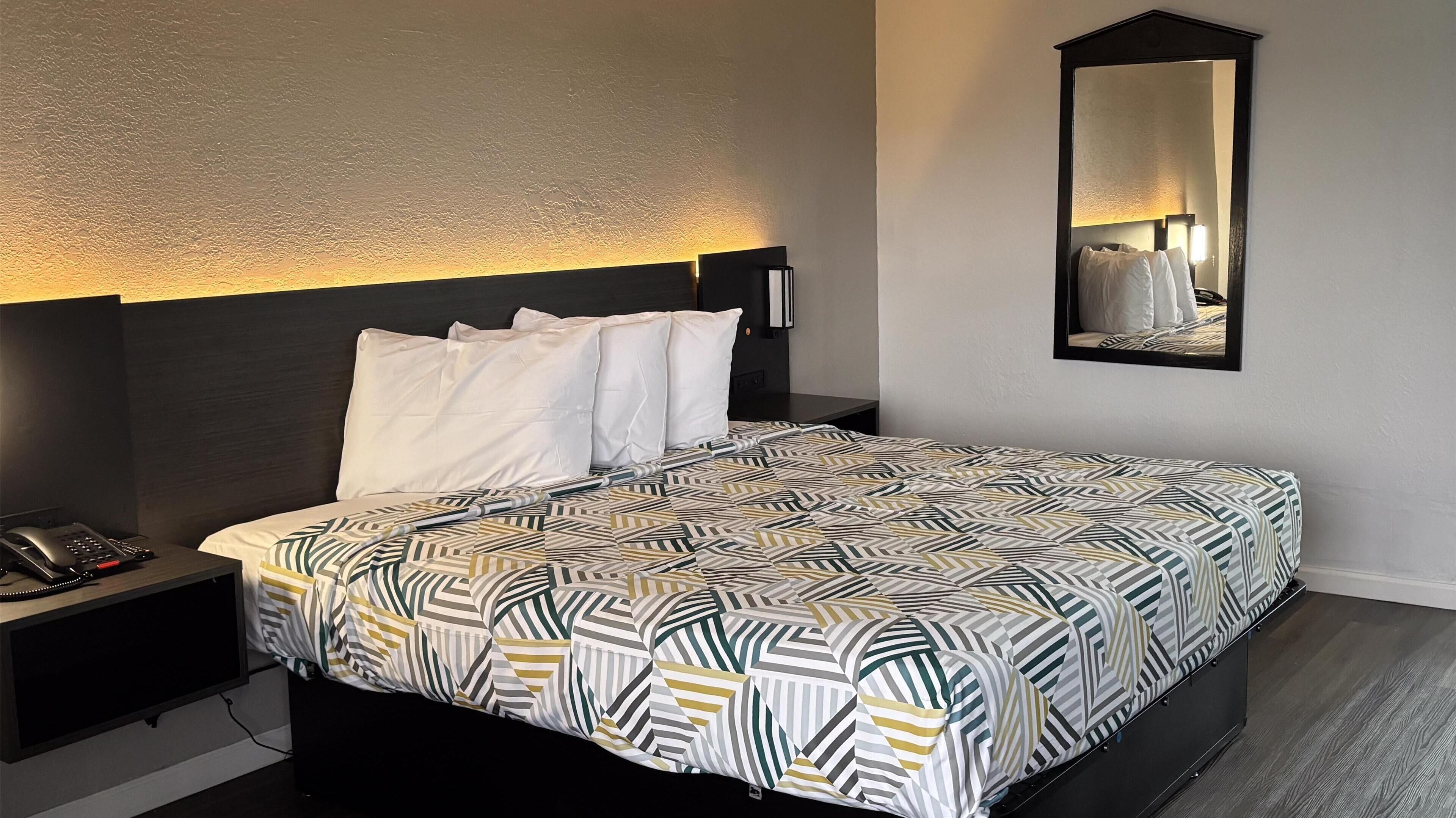 A hotel room with a bed, a bedside phone, a nightstand, a mirror, and a patterned bedspread.