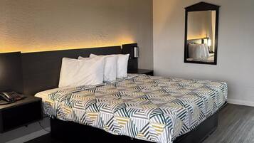 A hotel room with a bed, a bedside phone, a nightstand, a mirror, and a patterned bedspread.