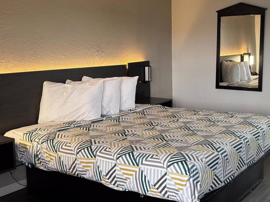 A hotel room with a bed, a bedside phone, a nightstand, a mirror, and a patterned bedspread.
