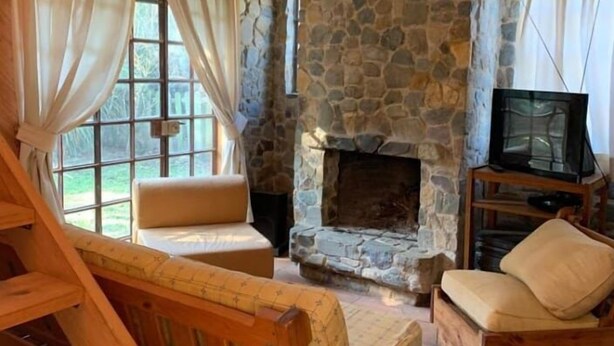 A cozy room with a stone fireplace, wooden furniture, and a television. - hermosa casa con piscina olmue (Olmue)