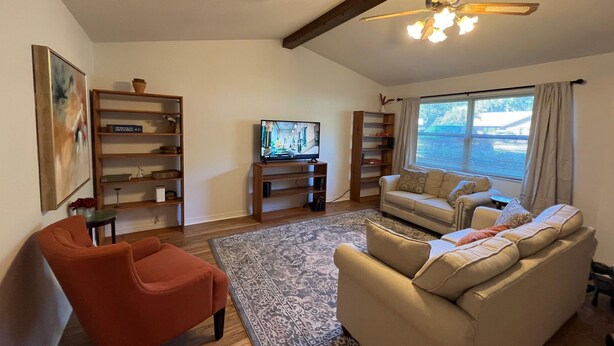 A living room with a television, a red armchair, a beige sofa, and wooden shelving units. - Cozy, Peaceful and Quiet Deerwood Cottage (Lake City)