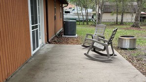 A concrete patio with two rocking chairs, a trash can, and a boat trailer in the background. - Cozy, Peaceful and Quiet Deerwood Cottage (Lake City)