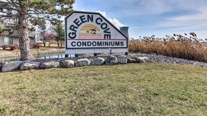 Naamplaatje voor Green Cove Condominiums met een helder uitzicht op het omliggende landschap, inclusief een vijver, bomen en een gebouw op de achtergrond.