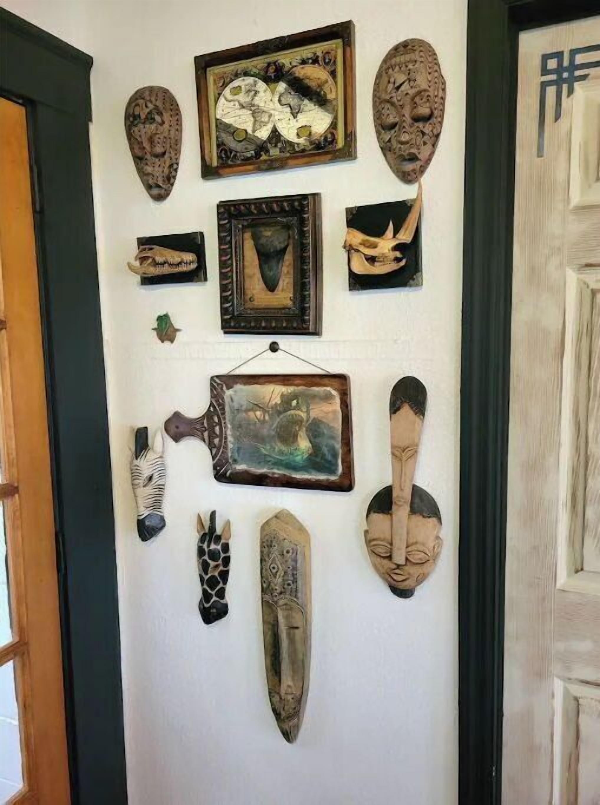 A wall with various cultural artifacts, including masks, a carved wooden figure, and a framed painting.