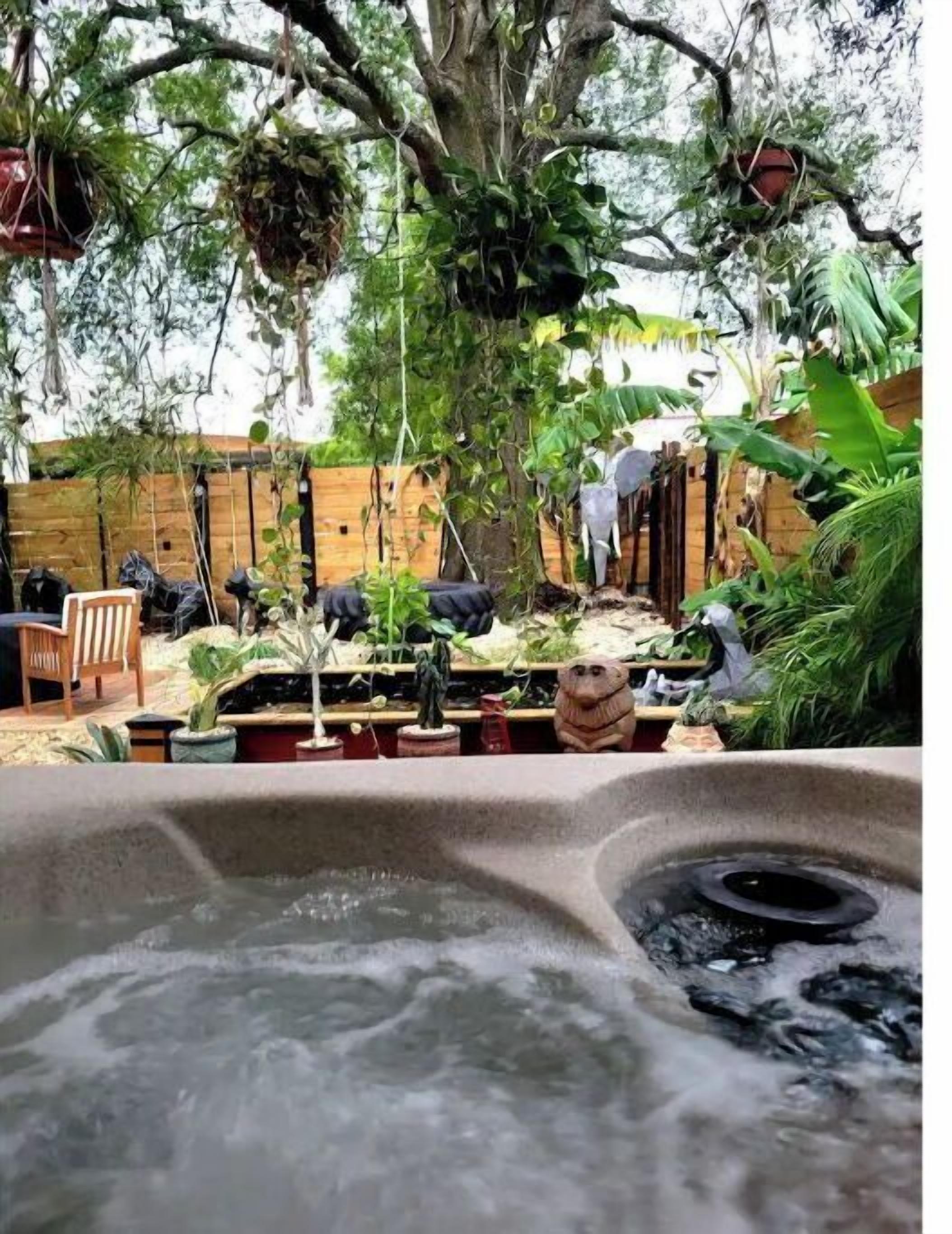 A hot tub with water, surrounded by potted plants and a wooden fence.