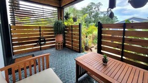 Een overdekt terras met houten meubels, potplanten en een patroonvloer.