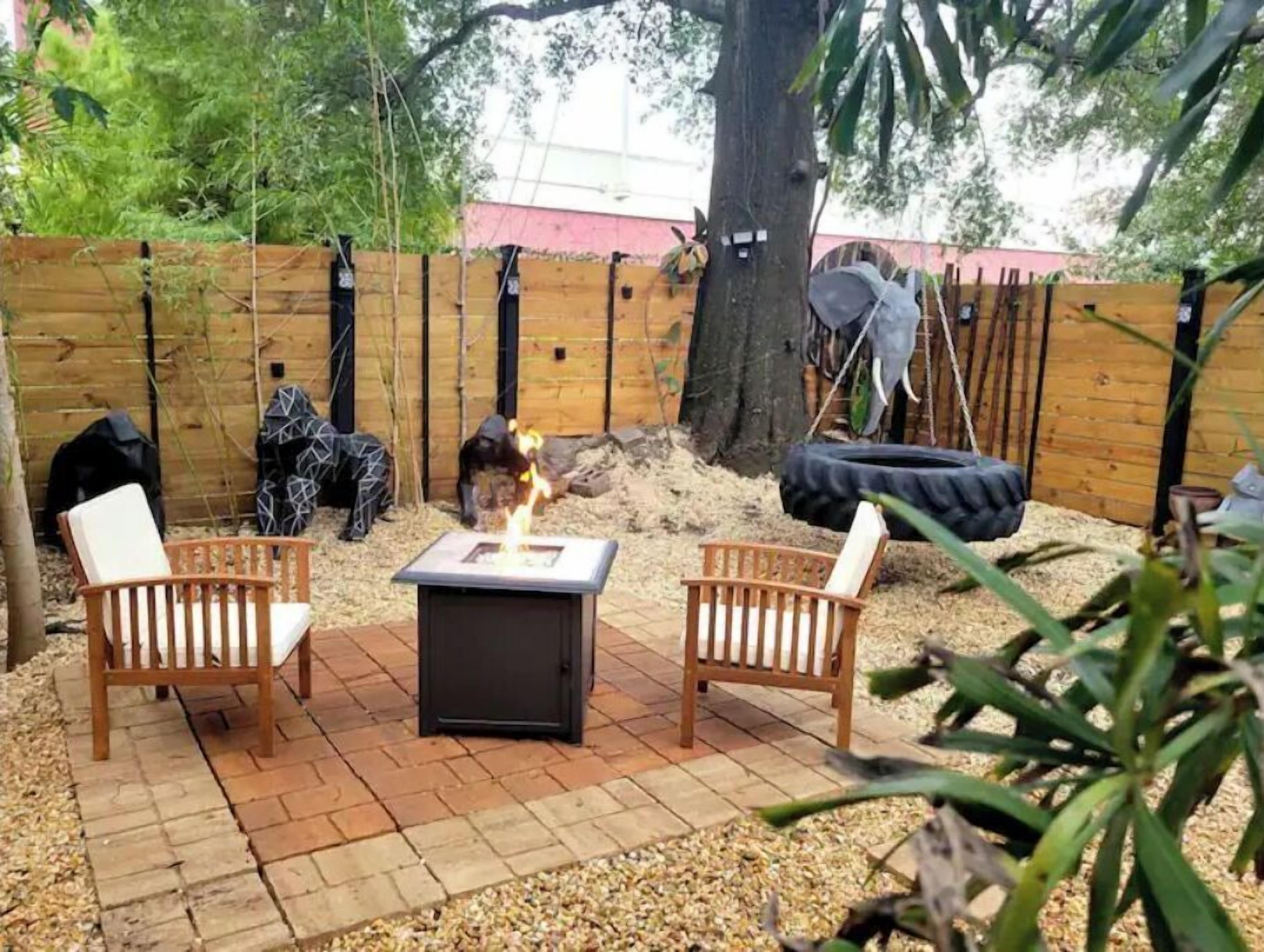 Een terras met twee houten stoelen, een vierkante tafel en een vuurkuil.