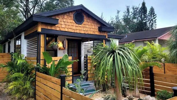 Een modern huis met een houten gevel, een overdekte veranda en een tuin met diverse planten en een kleine vijver.