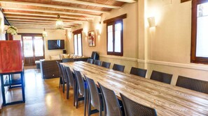 A long dining table with wicker chairs, a television mounted on the wall, and a wooden ceiling with exposed beams. - Le Chêne Creux Country House (Campillejo)