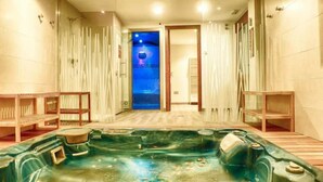 Une salle de spa équipée d’un bain à remous, de bancs en bois et offrant une vue sur un ciel bleu par une porte.