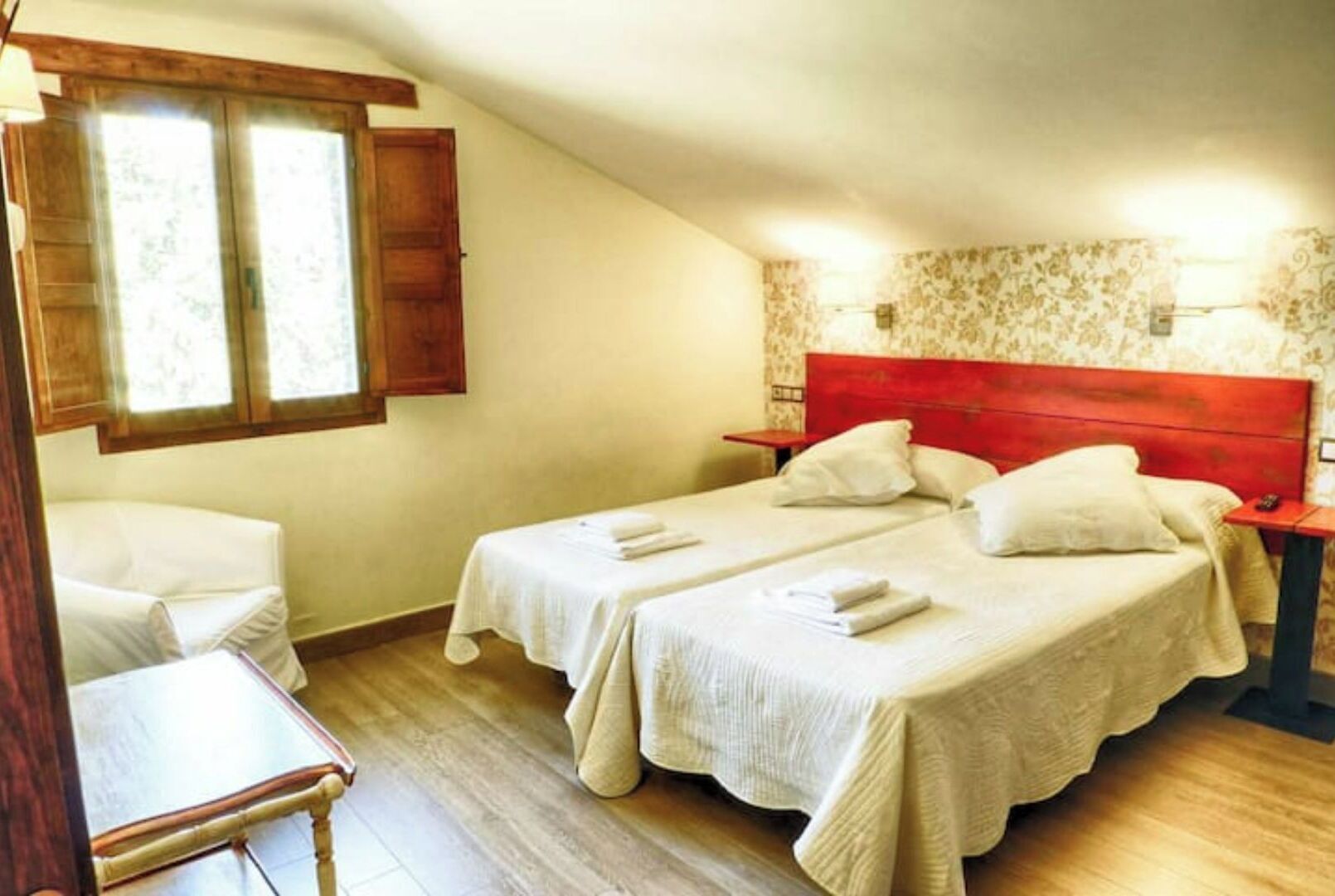 Un dormitorio con dos camas, una silla y suelo de madera.