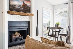 A cozy living room with a fireplace, a television mounted above it, and a dining area with a table and chairs.