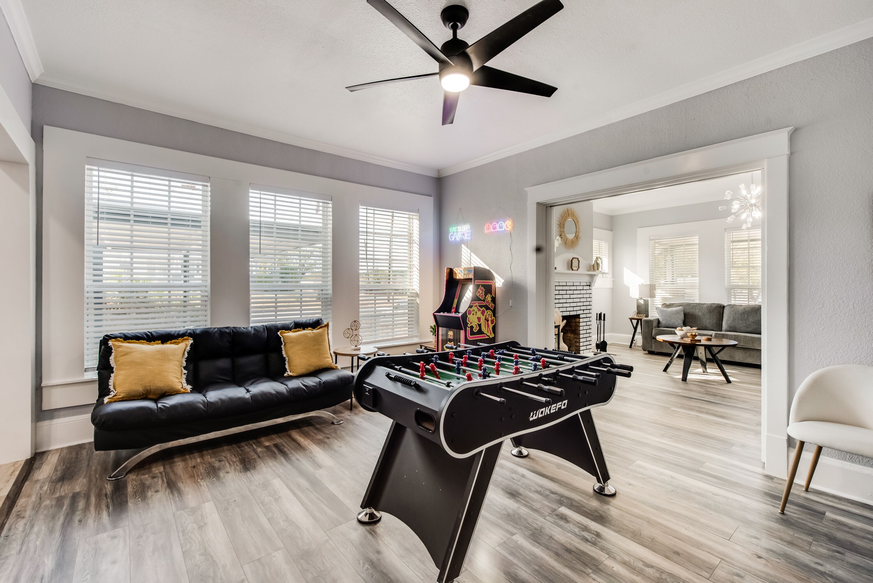 A spacious living room with a foosball table, a black leather sofa, and a ceiling fan.