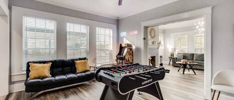 A spacious living room with a foosball table, a black leather sofa, and a ceiling fan.