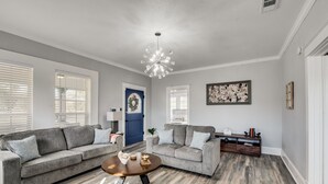 A modern living room with a grey sofa, a round coffee table, and a blue door. - Beautiful 1930s Mineral Wells Home, Near Downtown! (Mineral Welss)