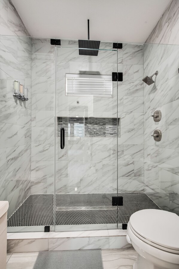 Un baño moderno con ducha de vidrio, inodoro y pared de mármol.