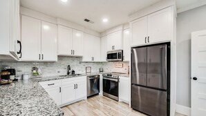 A modern kitchen with white cabinets, stainless steel appliances, and a granite countertop. - Beautiful 1930s Mineral Wells Home, Near Downtown! (Mineral Welss)