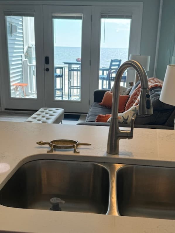 A kitchen with a stainless steel sink, a decorative spoon, and a view of the ocean through large sliding glass doors.