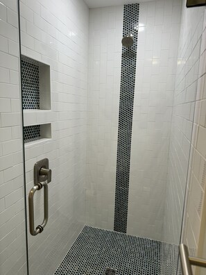 Une douche aux murs recouverts de carreaux blancs et ornée d’une bande verticale noire et blanche.