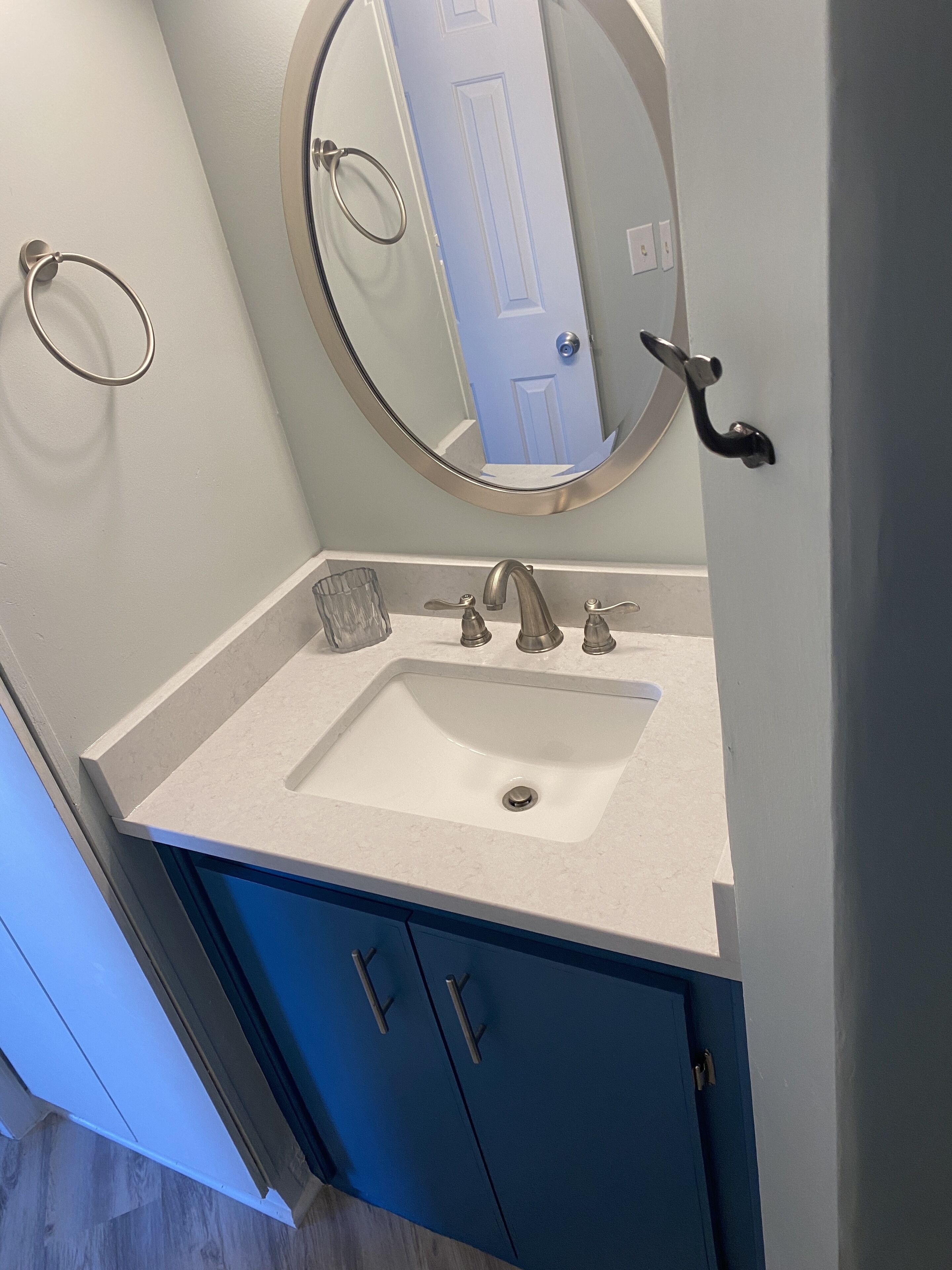 A bathroom with a white sink, a round mirror, and blue cabinets.