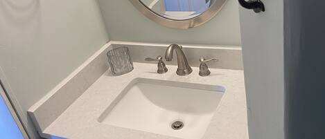 A bathroom with a white sink, a round mirror, and blue cabinets.