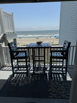 Une table et des chaises en bois sur une véranda, avec vue sur la plage et l’océan.
