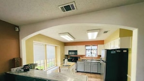 Una cocina con isla central, armarios blancos, un refrigerador negro y una ventana con persianas.