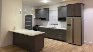 A modern kitchen with dark cabinets, a central island, stainless steel appliances, and pendant lighting. - The White House TCI Guests house (The Bight Settlement)