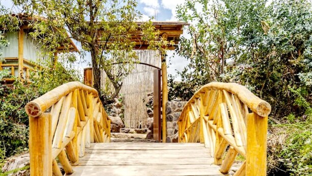 A wooden bridge leading to a traditional building with a stone base and a wooden roof. - Comfortable Villa in the Sacred Valley: Hot Tub, Sauna, Views of the Waterfall and Mountains (Calca)