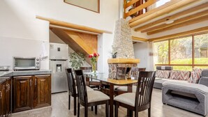 A modern kitchen with a stone fireplace, wooden ceiling beams, and a dining area with a sofa and chairs. - Comfortable Villa in the Sacred Valley: Hot Tub, Sauna, Views of the Waterfall and Mountains (Calca)