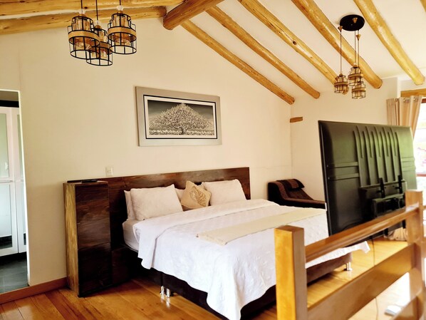 A bedroom with a wooden bed, white bedding, a framed picture on the wall, and a TV on a stand.