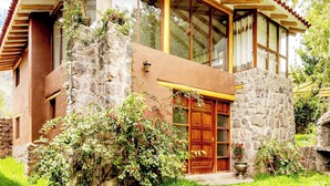 A stone building with a wooden door and windows, surrounded by greenery. - Comfortable Villa in the Sacred Valley: Hot Tub, Sauna, Views of the Waterfall and Mountains (Calca)