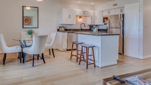 A modern kitchen with white cabinets, a central island with stools, and a ceiling fan.