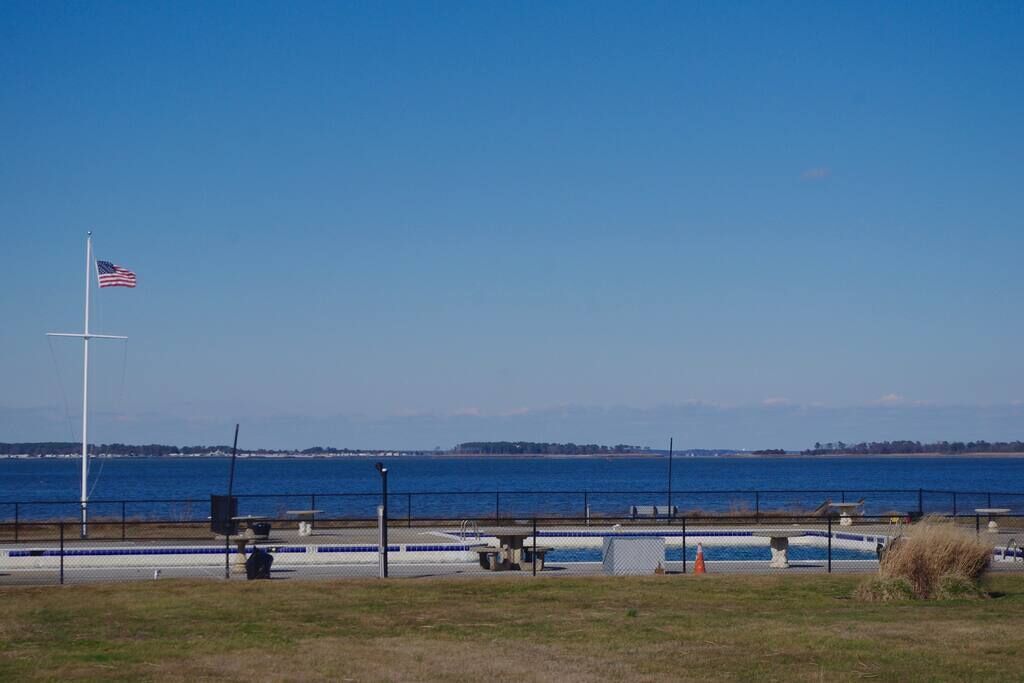 A waterfront view with a flagpole, a swimming pool, and a grassy area.