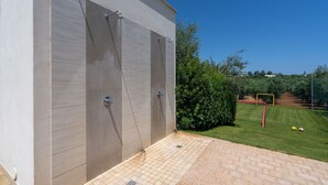 A modern outdoor shower area with a tiled floor and a grassy lawn with a soccer goal in the background. - Amazing Villa with Private Pool in Monopoli (Cozzana)