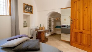 A bedroom with a bed, a wooden wardrobe, a radiator, a mirror, a window with curtains, and a small table with bottles. - Amazing Villa with Private Pool in Monopoli (Cozzana)