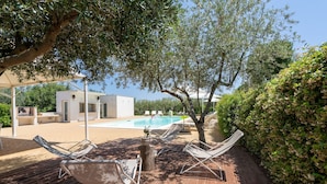 A wooden deck with lounge chairs, a pool, and a building in the background. - Amazing Villa with Private Pool in Monopoli (Cozzana)