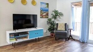 A living room with a flat-screen TV on a white cabinet, a potted plant, a gray armchair, and a window with curtains. - Lakefront Getaway |Private Dock + Free Kayaks (Bella Vista)