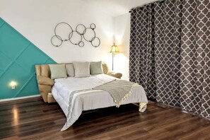A bedroom with a bed, a chair, a wall-mounted lamp, and patterned curtains. - Lakeside Trail (Bella Vista)