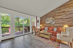 A spacious living room with a wooden accent wall, a red sofa, a striped armchair, and a coffee table. - Corner Lake Getaway (Bella Vista)