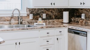 Una cocina con armarios blancos, encimera de granito, pileta de acero inoxidable, dispensador de jabón para lavar platos y soporte para toallas de papel.