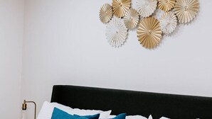 Una cama bien hecha con almohadas blancas y azules, cabecera negra y una pared con motivos circulares decorativos.
