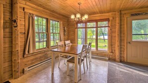 A wooden cabin interior with a dining table, chairs, large windows, and a chandelier. - Cozy Riverfront Getaway: Fishing On-Site! (Lacon)