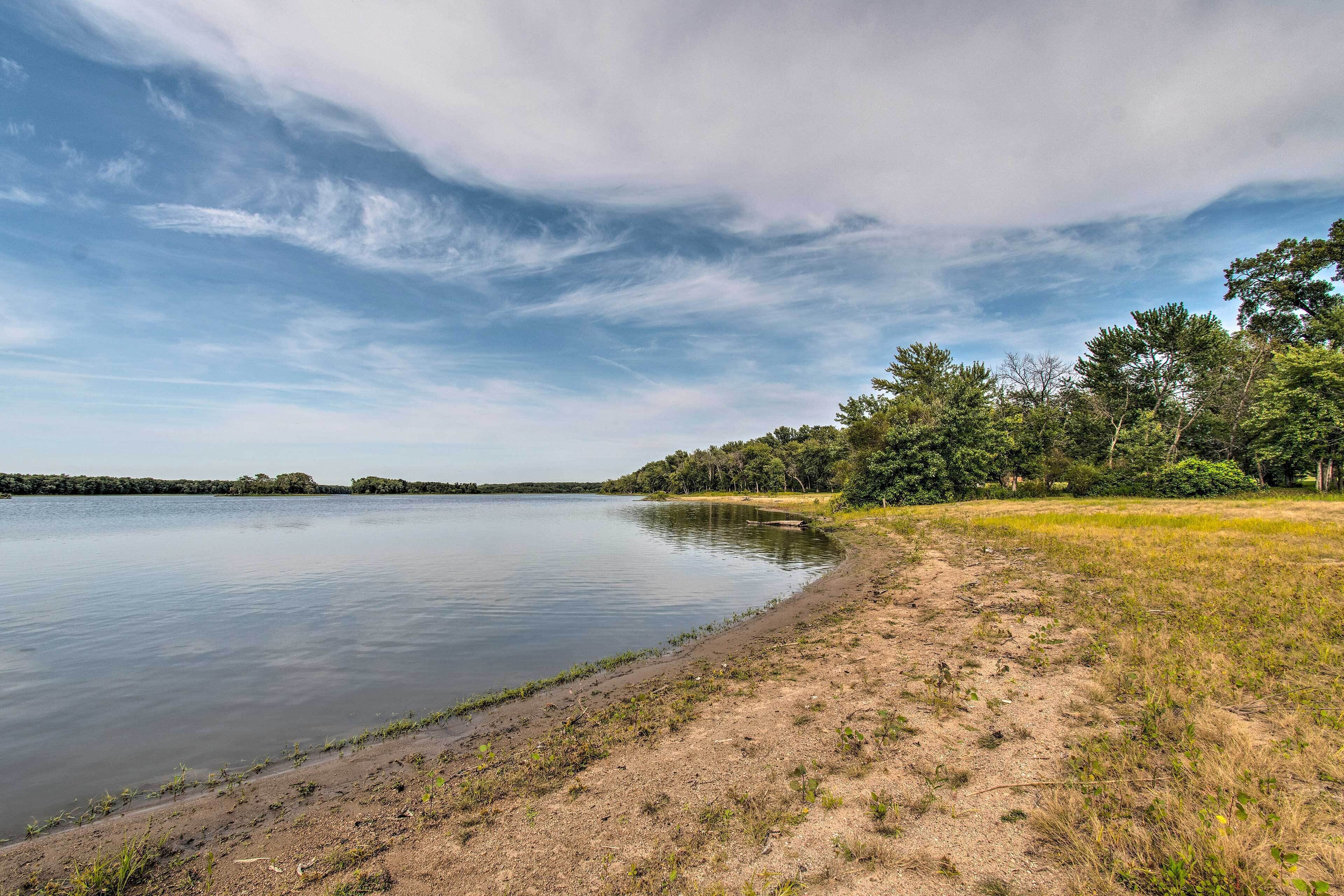 Ein ruhiger See mit sandigem Ufer und Bäumen im Hintergrund.