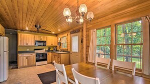 A wooden cabin kitchen with a dining table, chairs, and a chandelier. - Cozy Riverfront Getaway: Fishing On-Site! (Lacon)