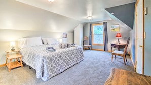 A bedroom with a bed, bedside table, chair, desk, and window.